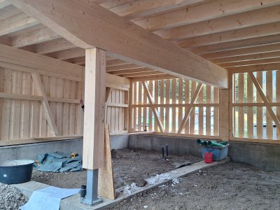 In einem Rahmen aus Holz findet eine Bauaktivität statt. Der Boden ist vorbereitet und Baustellenutensilien sind sichtbar.