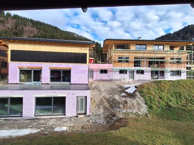 Neue Gebäude werden in den Bergen gebaut. Der Himmel ist teilweise bewölkt. Es gibt Baumaterialien und Erde um die Baustelle.