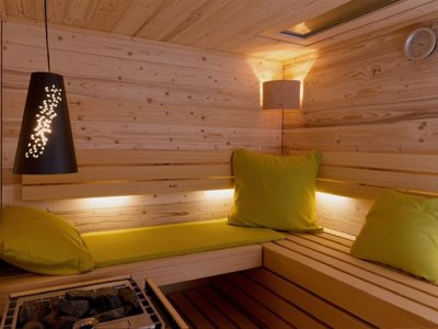 In einem warmen Raum sind Holz und Kissen zu sehen. Menschen sitzen und entspannen sich in der Sauna.
