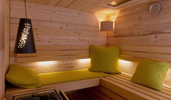 In einem warmen Raum sind Holz und Kissen zu sehen. Menschen sitzen und entspannen sich in der Sauna.