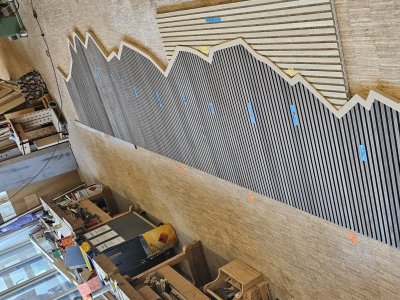In einer Werkstatt liegen Holzplatten auf dem Boden. Sie sind länger und haben verschiedene Muster. Arbeiter planen die Montage.