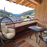 Loggia in Suite Die Sieben Auf dem Balkon stehen ein Tisch und zwei Stühle. Ein Hängesessel ist bereit zum Entspannen. Die Berge sind im Hintergrund sichtbar.
