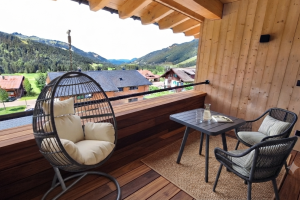 Auf dem Balkon stehen ein Tisch und zwei Stühle. Ein Hängesessel ist bereit zum Entspannen. Die Berge sind im Hintergrund sichtbar.