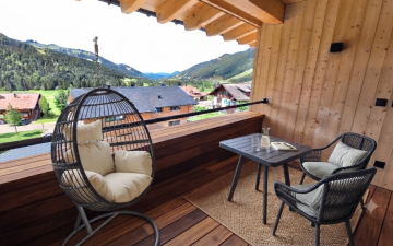 Loggia in Suite Die Sieben Auf dem Balkon stehen ein Tisch und zwei Stühle. Ein Hängesessel ist bereit zum Entspannen. Die Berge sind im Hintergrund sichtbar.