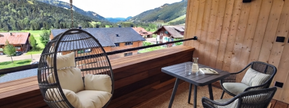 Loggia in Suite Die Sieben Auf dem Balkon stehen ein Tisch und zwei Stühle. Ein Hängesessel ist bereit zum Entspannen. Die Berge sind im Hintergrund sichtbar.