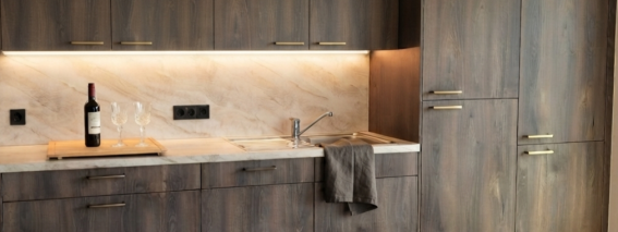 Moderne Küche in Suite SIEBEN In einem Raum mit Holzschränken und Steinarbeiten stehen Flasche und Gläser auf der Arbeitsfläche in der Küche.