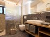Modernes Badezimmer in einem Holzhaus Das Badezimmer hat eine Steinwand, eine Dusche und einen Holzschrank. Es gibt einen Spiegel und ein Fenster.