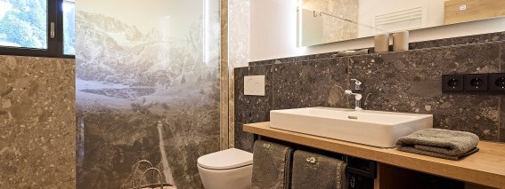 Modernes Badezimmer in einem Holzhaus Das Badezimmer hat eine Steinwand, eine Dusche und einen Holzschrank. Es gibt einen Spiegel und ein Fenster.