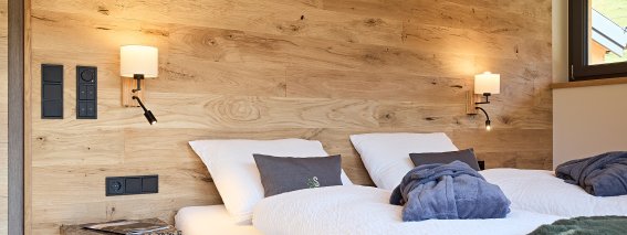 Gemütlicher Raum mit zwei Betten in einem Holzhaus Zwei getrennte Betten stehen in einem Raum mit Holzwand. Es gibt Lampen und eine kleine Ablage.