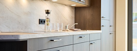Moderne Küche mit Möbeln in neutralen Farben Eine Küche mit grauen und holzfarbenen Schränken steht im Raum. Die Arbeitsplatte ist aus Marmor.