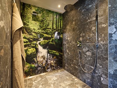 In einem modernen Badezimmer steht eine Dusche mit grauen Fliesen. An der Wand ist ein Motiv eines Waldes mit einem Fluss.