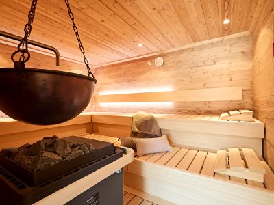 In einem Holzraum gibt es eine Sauna mit Bänken und einem heißen Ofen. Die Steine liegen bereit zum Aufguss.