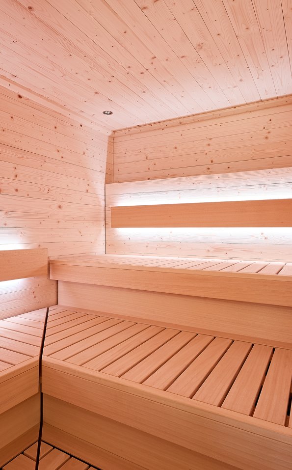 In diesem Raum sind Wände und Bänke aus Holz. Sanfte Lichter sorgen für eine ruhige Atmosphäre ohne Menschen.