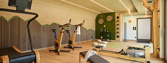 In einem modernen Fitnessraum stehen Laufband, Fahrräder und eine Trainingsbank bereit. Viel Platz für Fitness und Training.