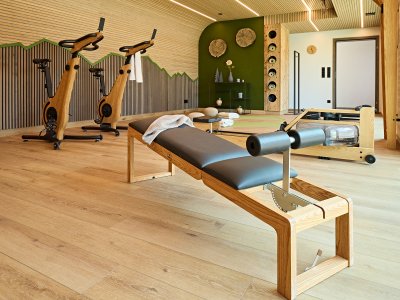 In einem modernen Fitnessraum stehen zwei Trainingsgeräte. Ein Pilates-Reformer liegt bereit zum Üben.