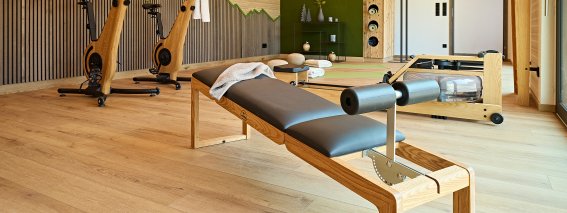 In einem modernen Fitnessraum stehen zwei Trainingsgeräte. Ein Pilates-Reformer liegt bereit zum Üben.