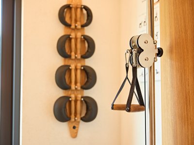 Im Raum sind verschiedene Trainingsgeräte zu sehen. An der Wand hängen Gewichte und eine Rolle mit einer Zugvorrichtung.