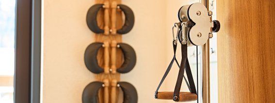 Im Raum sind verschiedene Trainingsgeräte zu sehen. An der Wand hängen Gewichte und eine Rolle mit einer Zugvorrichtung.