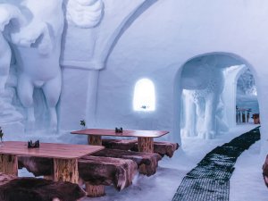 Ein Raum aus Schnee hat Holzstühle und Tische. Die Wände sind aus Eis und Figuren sind sichtbar.