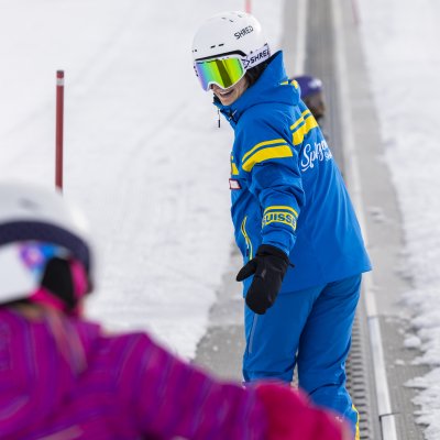 Ein Skilehrer zeigt Kindern die Grundlagen des Skifahrens auf einer verschneiten Piste an einem sonnigen Tag.