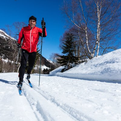 Ein Langläufer genießt eine entspannte Tour auf einer schneebedeckten Strecke in den Bergen an einem sonnigen Wintertag.