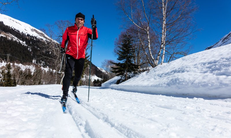Ein Langläufer genießt eine entspannte Tour auf einer schneebedeckten Strecke in den Bergen an einem sonnigen Wintertag.
