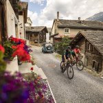 Runda Laida Vons Zwei Radfahrer fahren durch ein charmantes Dorf in den Bergen an einem sonnigen Tag im Sommer.