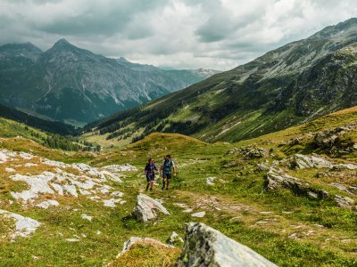 Zwei Wanderer gehen auf einem Pfad durch die grünen Berge an einem bewölkten Tag.