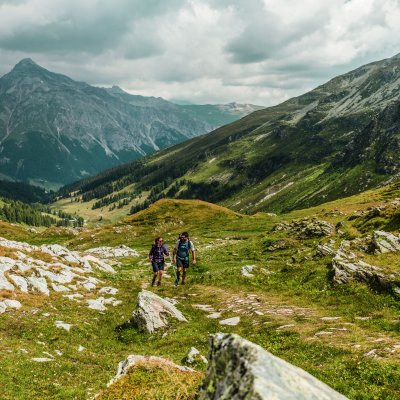 Zwei Wanderer gehen auf einem Pfad durch die grünen Berge an einem bewölkten Tag.