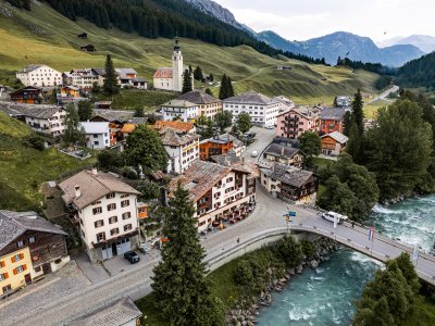 Idyllische Landschaft mit einem kleinen Dorf und grünen Bergen im Sommer, umgeben von einer ruhigen Flusslandschaft.