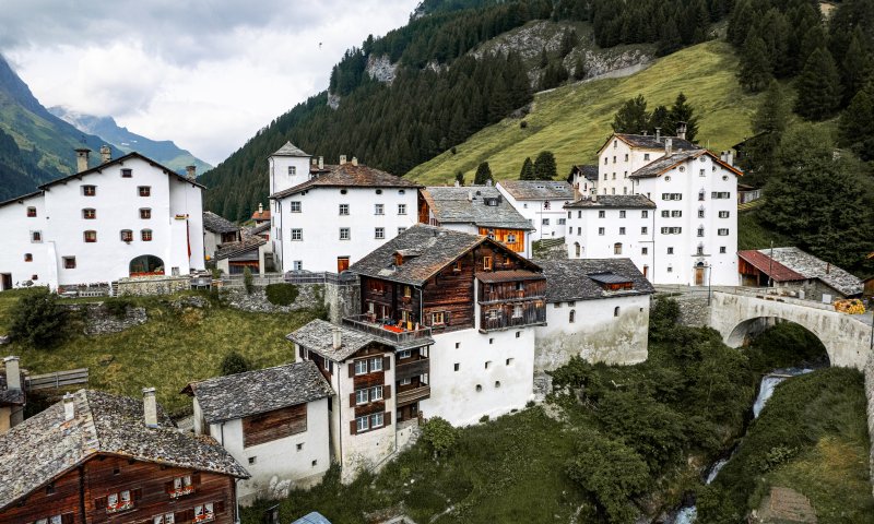 In einem ruhigen Bergdorf sind alte Häuser auf grünen Hügeln zu sehen. Der Himmel ist bewölkt und die Landschaft ist friedlich.