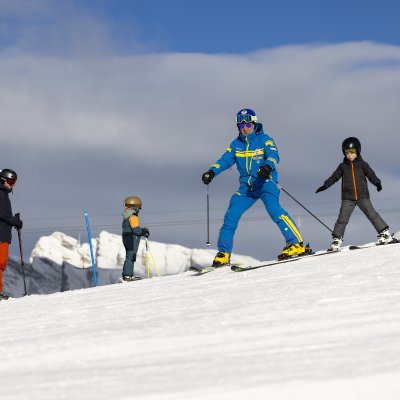 Eine Gruppe von Skifahrern geniesst einen sonnigen Tag in den Bergen. Kinder lernen Ski fahren mit einem Lehrer.