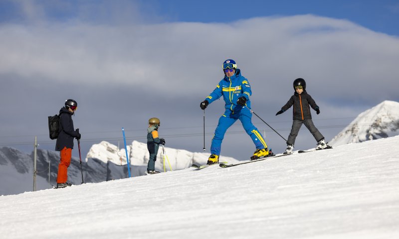 Eine Gruppe von Skifahrern geniesst einen sonnigen Tag in den Bergen. Kinder lernen Ski fahren mit einem Lehrer.
