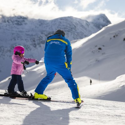 Ein Skilehrer zeigt einem kleinen Mädchen das Skifahren in den Bergen an einem sonnigen Tag.
