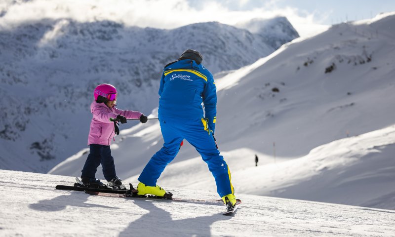 Ein Skilehrer zeigt einem kleinen Mädchen das Skifahren in den Bergen an einem sonnigen Tag.