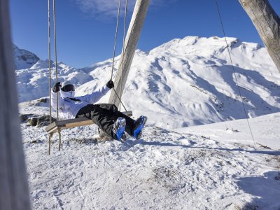 Eine Person schaukelt entspannt in den verschneiten Bergen während eines sonnigen Wintertags.