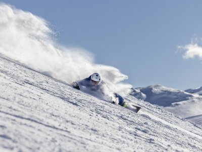 Ein Schneebrettfahrer fährt schnell den schneebedeckten Hang hinunter. Die Sonne scheint und der Schnee spritzt auf.