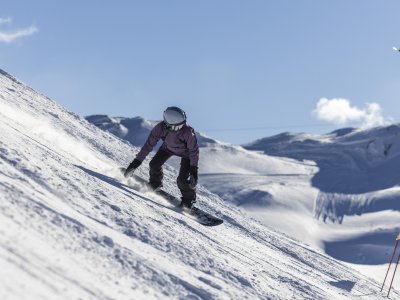 Ein Snowboardfahrer fährt auf einer schneebedeckten Piste in den Alpen bei sonnigem Wetter und klarer Sicht.