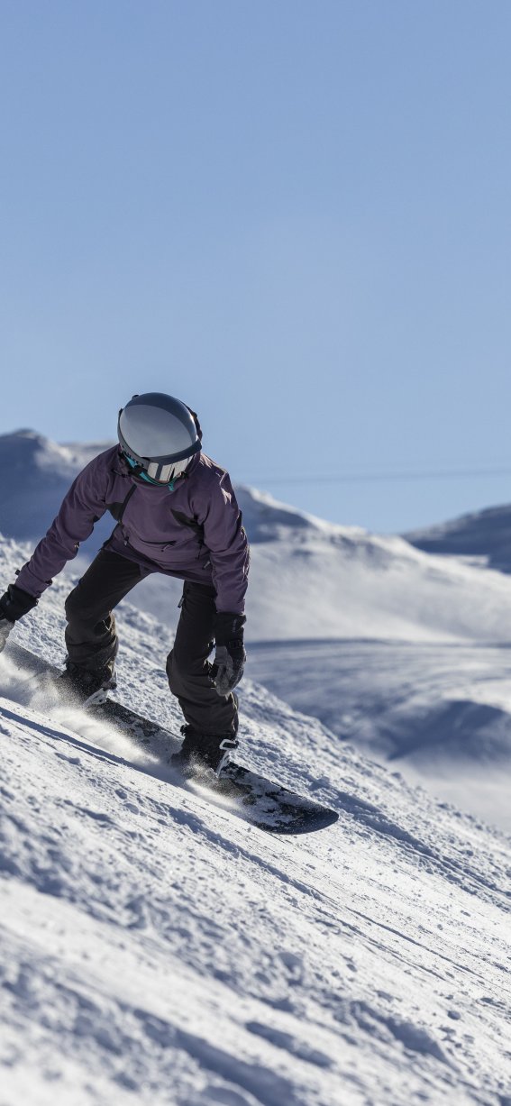Ein Snowboardfahrer fährt auf einer schneebedeckten Piste in den Alpen bei sonnigem Wetter und klarer Sicht.