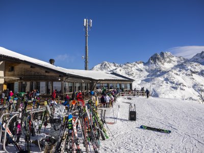 Die Skihütte ist voll mit Skifahrern, die sich nach dem Fahren entspannen, während die Sonne scheint und die Berge zu sehen sind.