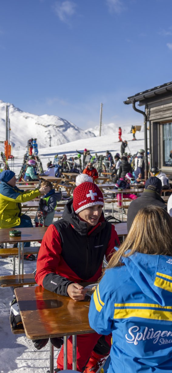 Gruppen von Menschen entspannen in einem Skigebiet, während sie die Aussicht und das Essen genießen. Es scheint Winter zu sein.
