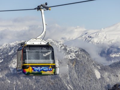 Eine farbenfrohe Bergbahn schwebt über schneebedeckte Berge und bietet einen wunderschönen Blick auf die alpine Landschaft.