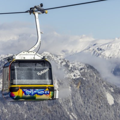 Eine farbenfrohe Bergbahn schwebt über schneebedeckte Berge und bietet einen wunderschönen Blick auf die alpine Landschaft.