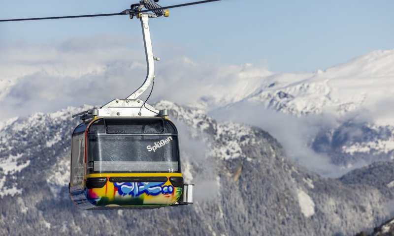 Eine farbenfrohe Bergbahn schwebt über schneebedeckte Berge und bietet einen wunderschönen Blick auf die alpine Landschaft.
