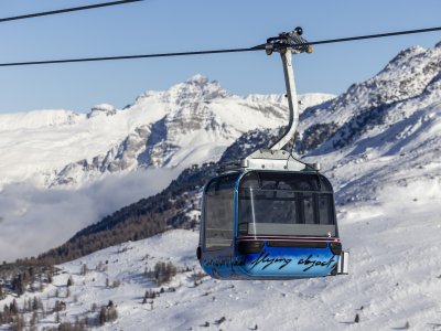 Eine Seilbahn schwebt über die verschneiten Alpen in einem klaren Himmel. Die Landschaft zeigt majestätische Berge und Winterdetails.