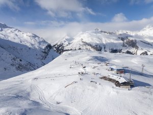 Viele Schneehügel und eine Skistation in den Bergen bei strahlend blauem Himmel. Es ist Winter und die Sonne scheint.