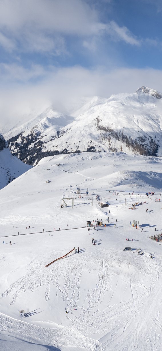 Viele Schneehügel und eine Skistation in den Bergen bei strahlend blauem Himmel. Es ist Winter und die Sonne scheint.