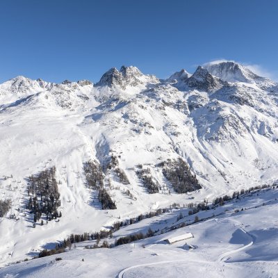 Die schneebedeckten Alpen strahlen unter blauem Himmel, während ein Skigebiet für Aktivitäten einladet.