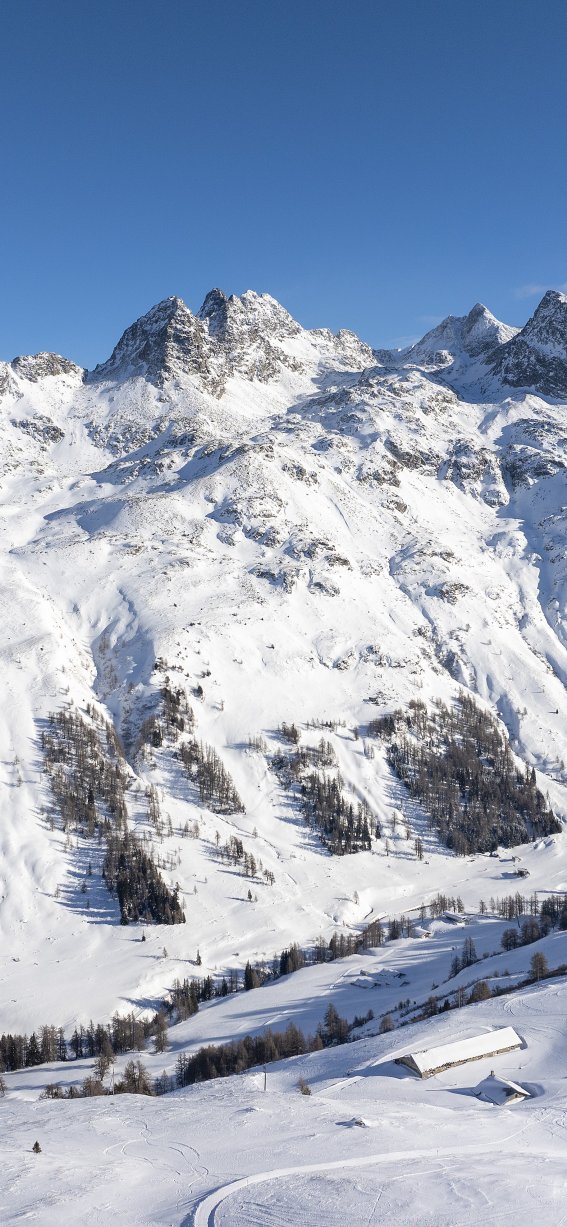 Die schneebedeckten Alpen strahlen unter blauem Himmel, während ein Skigebiet für Aktivitäten einladet.