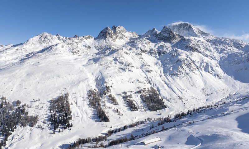 Die schneebedeckten Alpen strahlen unter blauem Himmel, während ein Skigebiet für Aktivitäten einladet.